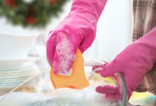 Manos de mujer con guantes sosteniendo Esponja Cero Rayas y lavando plato de cristal.